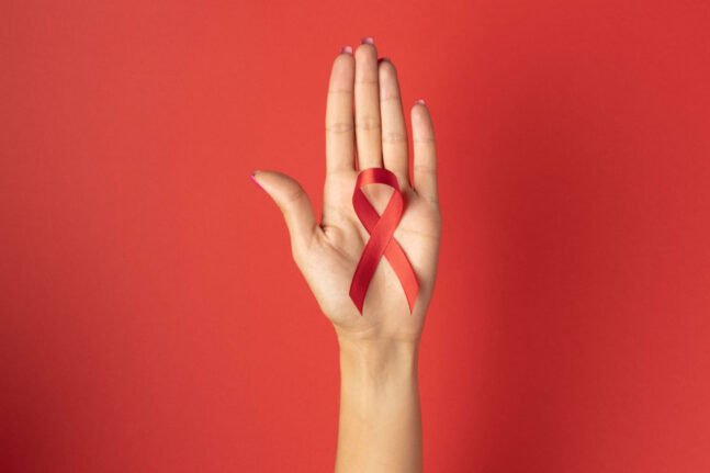 Fundo vermelho e uma mão branca aberta, centralizada, com um laço vermelho na palma da mão.