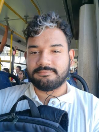 Fotografia de Fabrício. Jovem estudante, com barba cheia, em selfie sentado em um ônibus. A mochila está em seu colo.